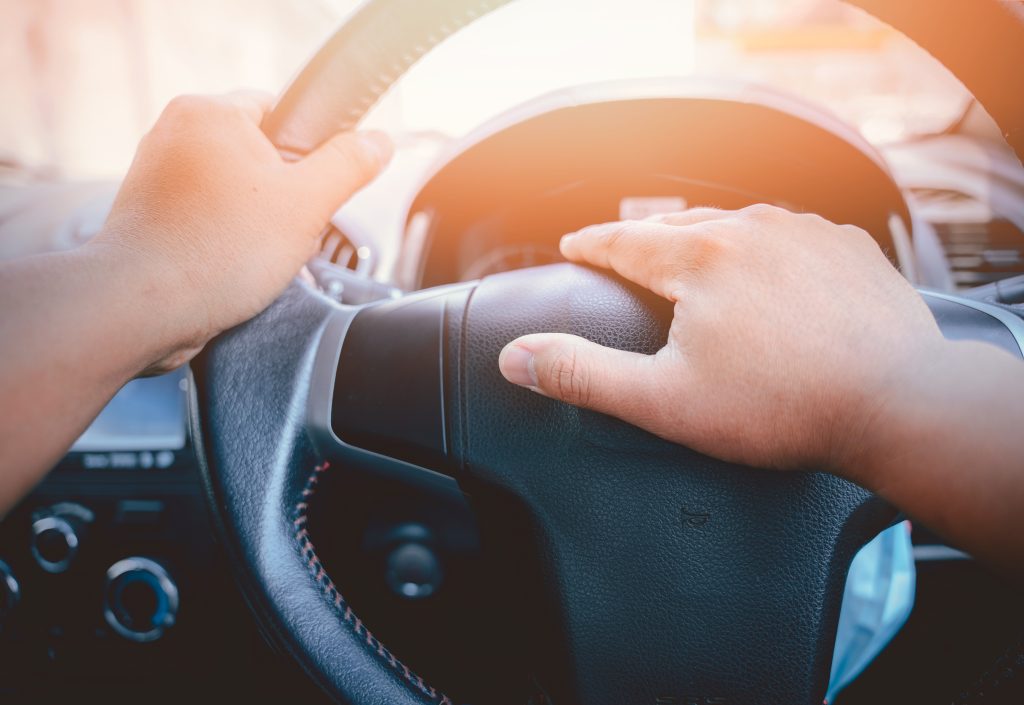 A close-up of a steering wheel with a hand on the horn